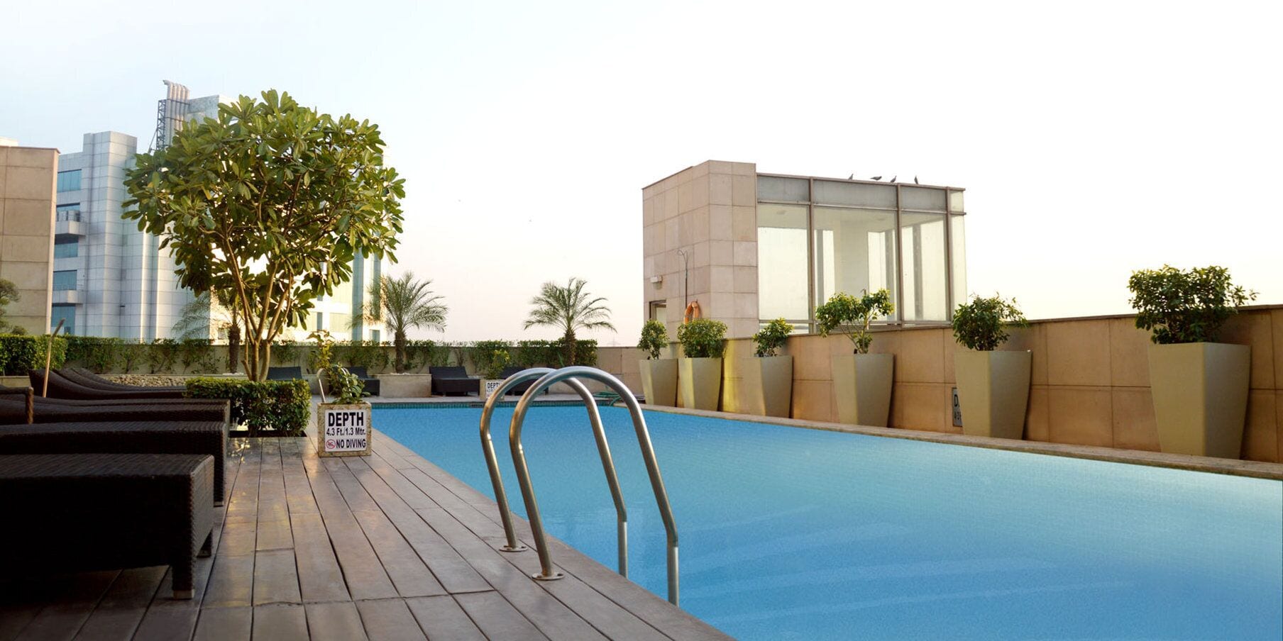A swimming pool with a depth sign, lounge chairs, and a modern building in the background.