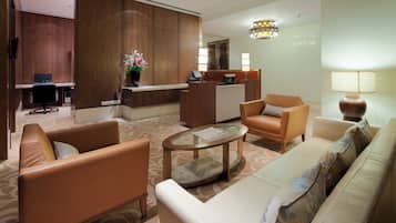 A hotel lobby with a reception desk, seating area with sofas and armchairs, a coffee table, and a decorative vase with flowers.