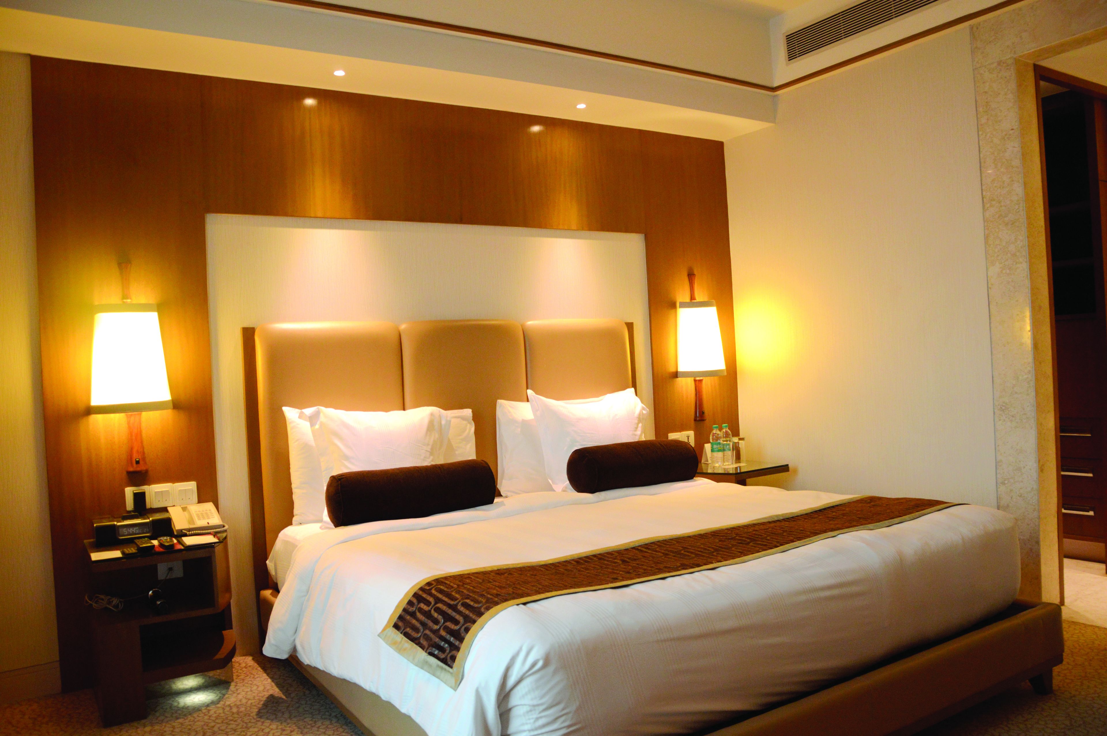 A hotel room with a large bed, two bedside lamps, a nightstand with a phone and a lamp, and a wooden headboard.