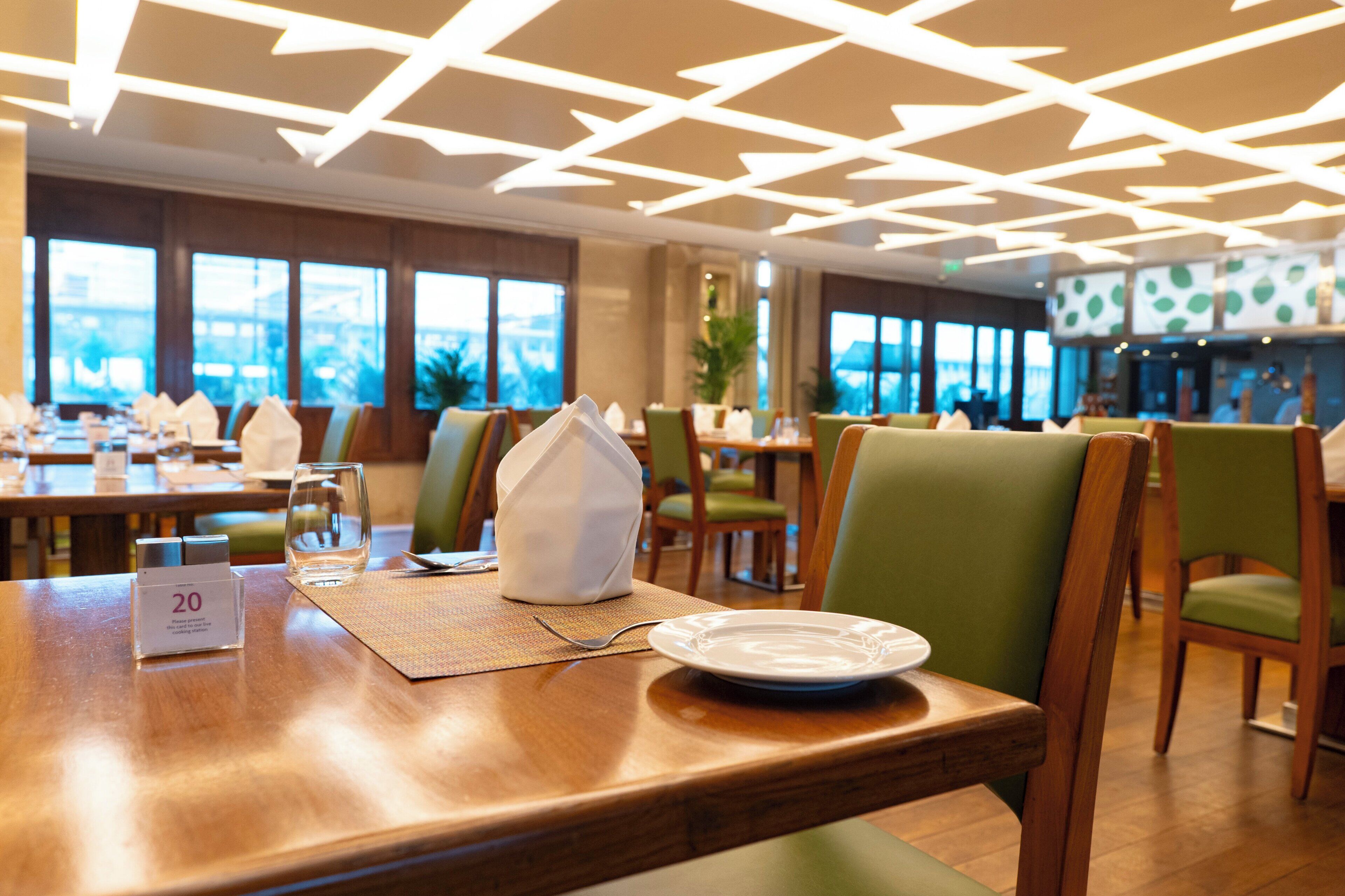 A restaurant with a modern ceiling design, wooden tables, and green upholstered chairs.