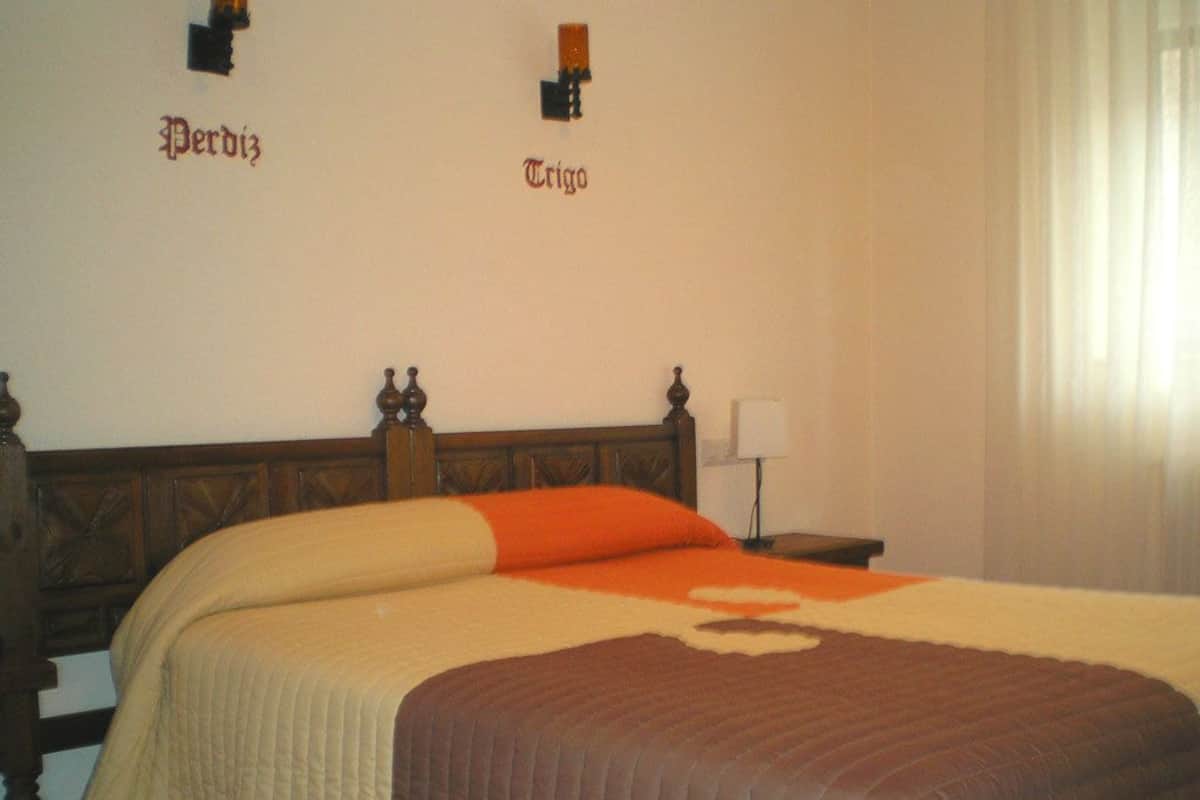 Una habitación de hotel con una cama grande, una mesita de noche, una lámpara y una ventana con cortinas.