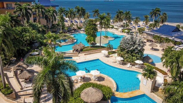 Et resort med flere swimmingpools, palmer og udsigt over havet.