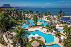 A resort with multiple swimming pools, palm trees, and a view of the ocean.