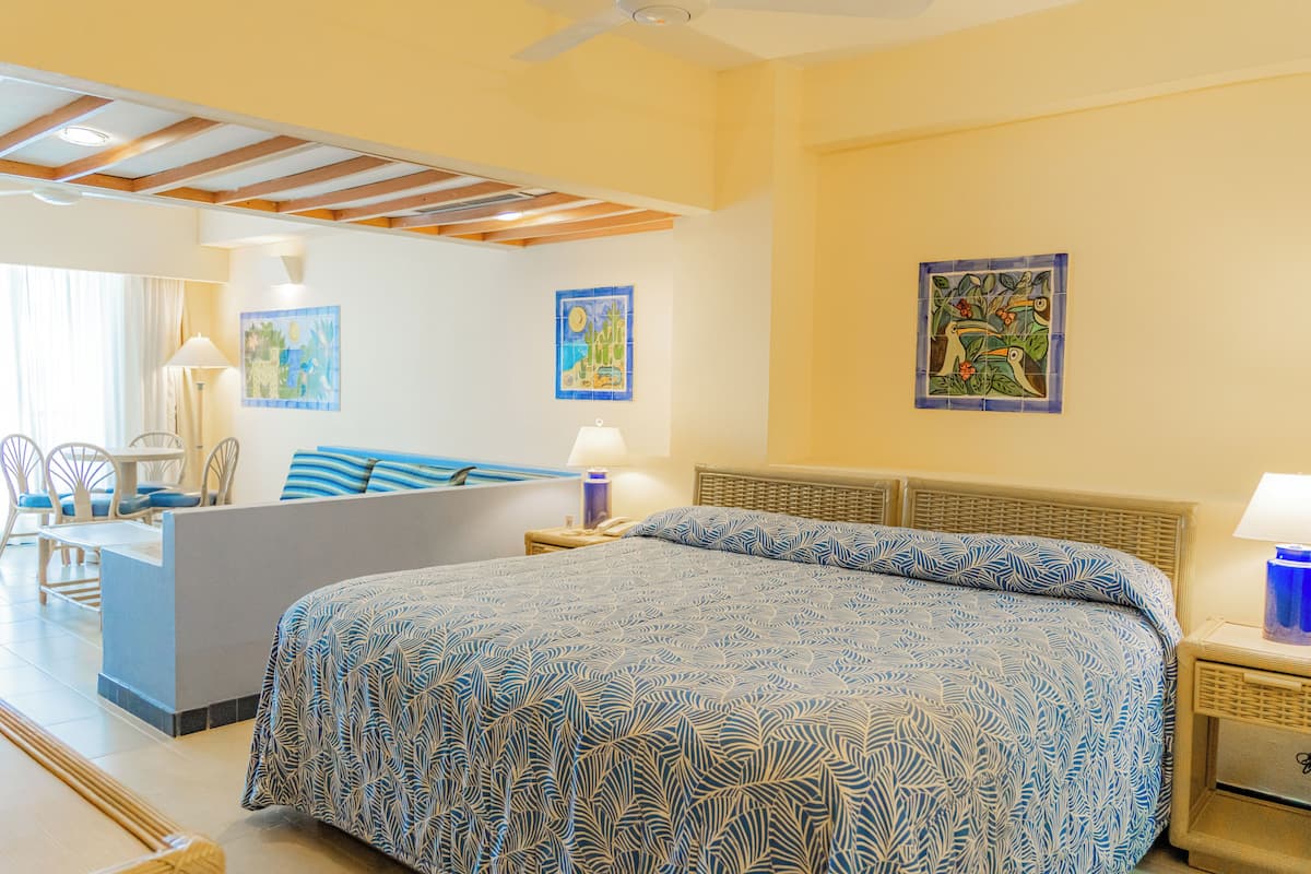 A hotel room with a bed, a sofa, a dining area, and artwork on the walls.