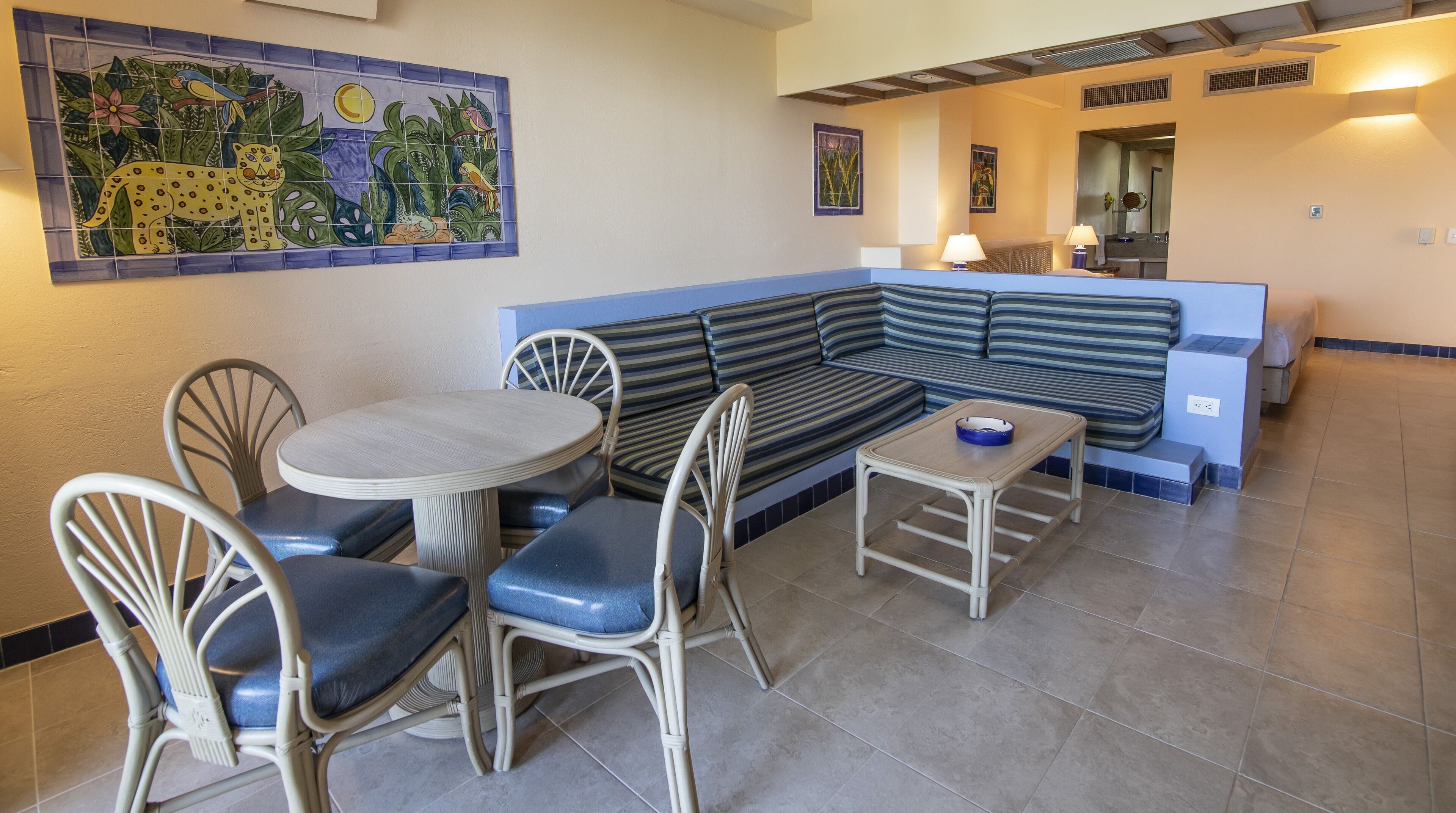 A dining area with a round table, four chairs, a striped sofa, and a small table with a bowl.