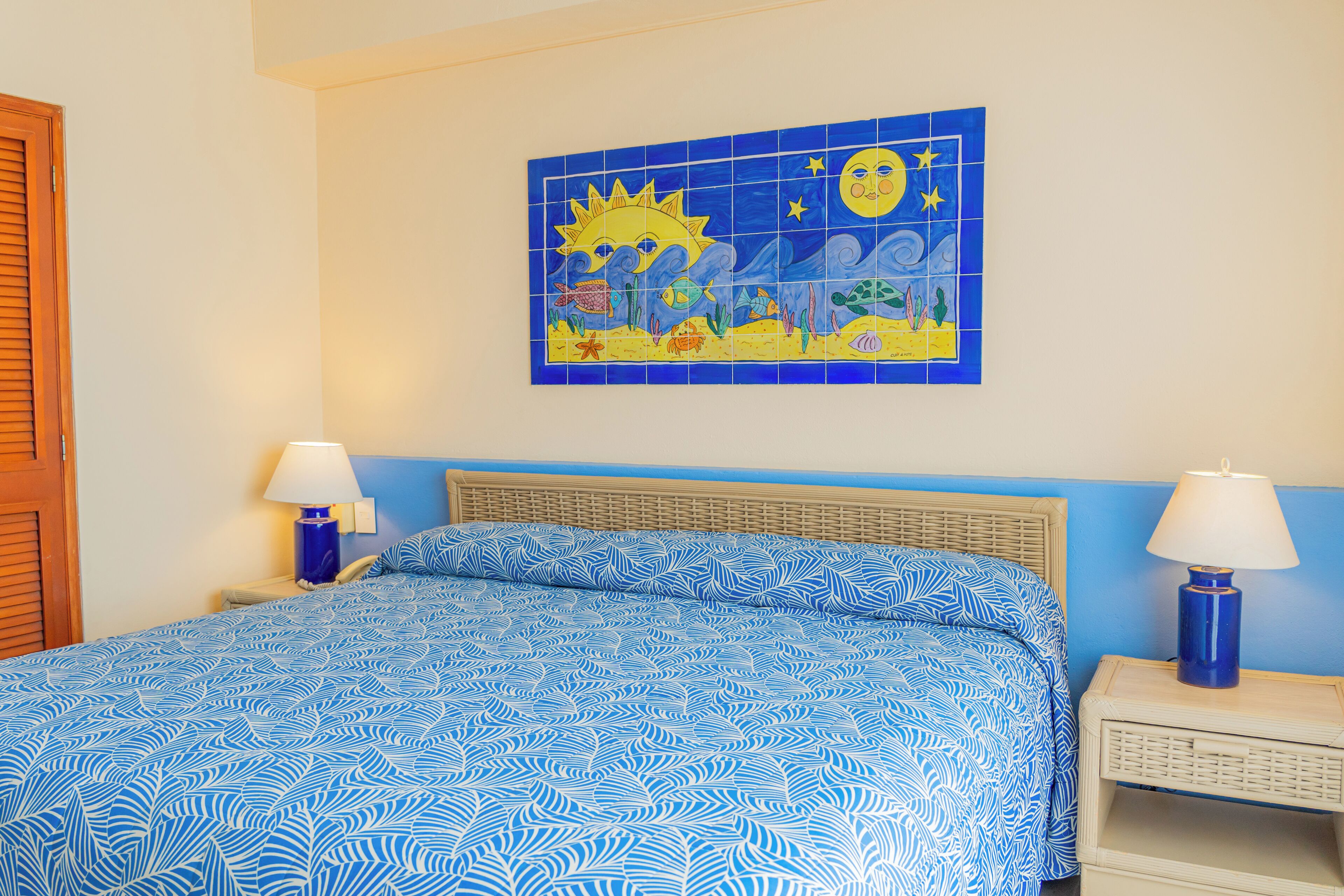 Un dormitorio con una colcha azul estampada, un mural en la pared y dos lámparas de noche.