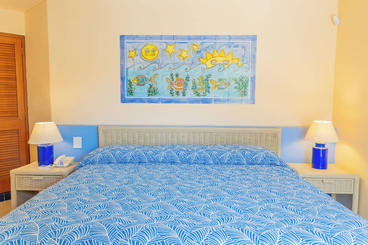 A hotel room with a bed, two bedside tables, a wall mural, and a wooden door.