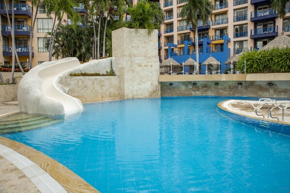 A swimming pool with a curved slide, surrounded by a poolside area with lounge chairs and umbrellas.