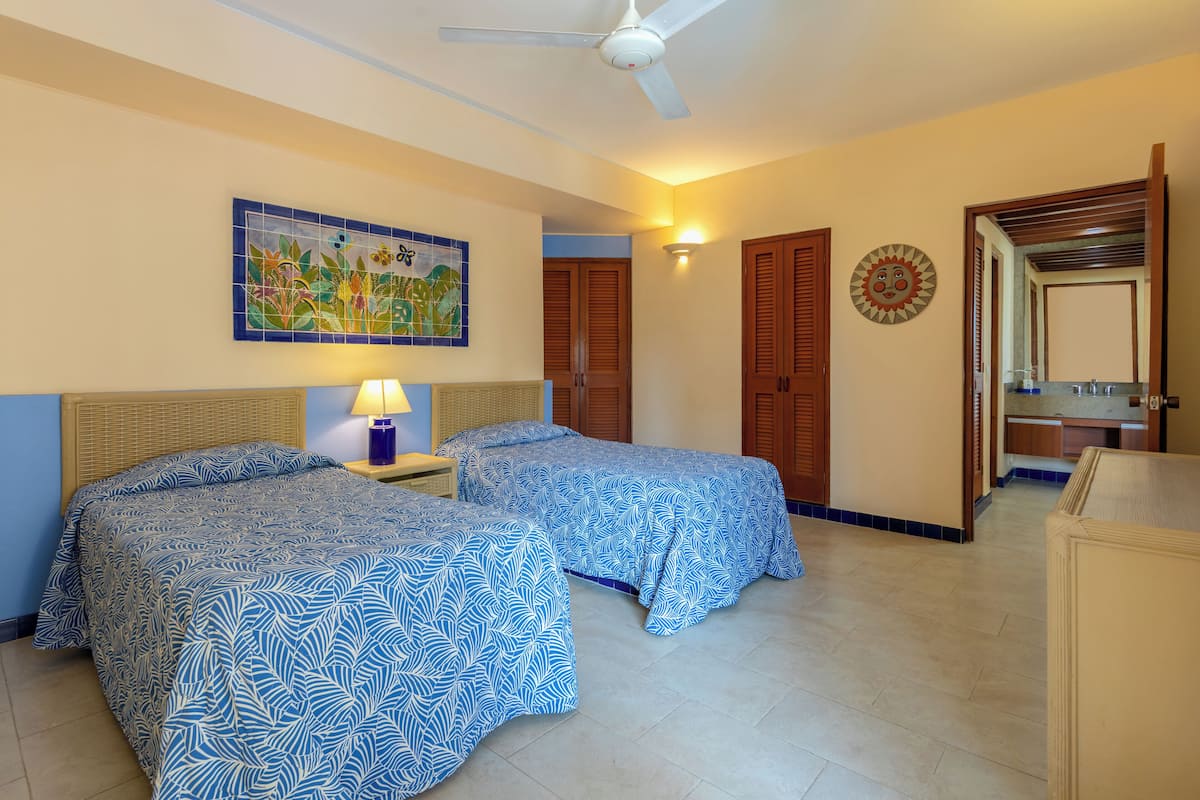 A room with two beds, a ceiling fan, a wall-mounted lamp, and a decorative tile.