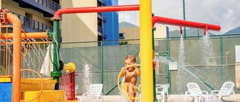 A water play area with a child playing, a pool, and lounge chairs.