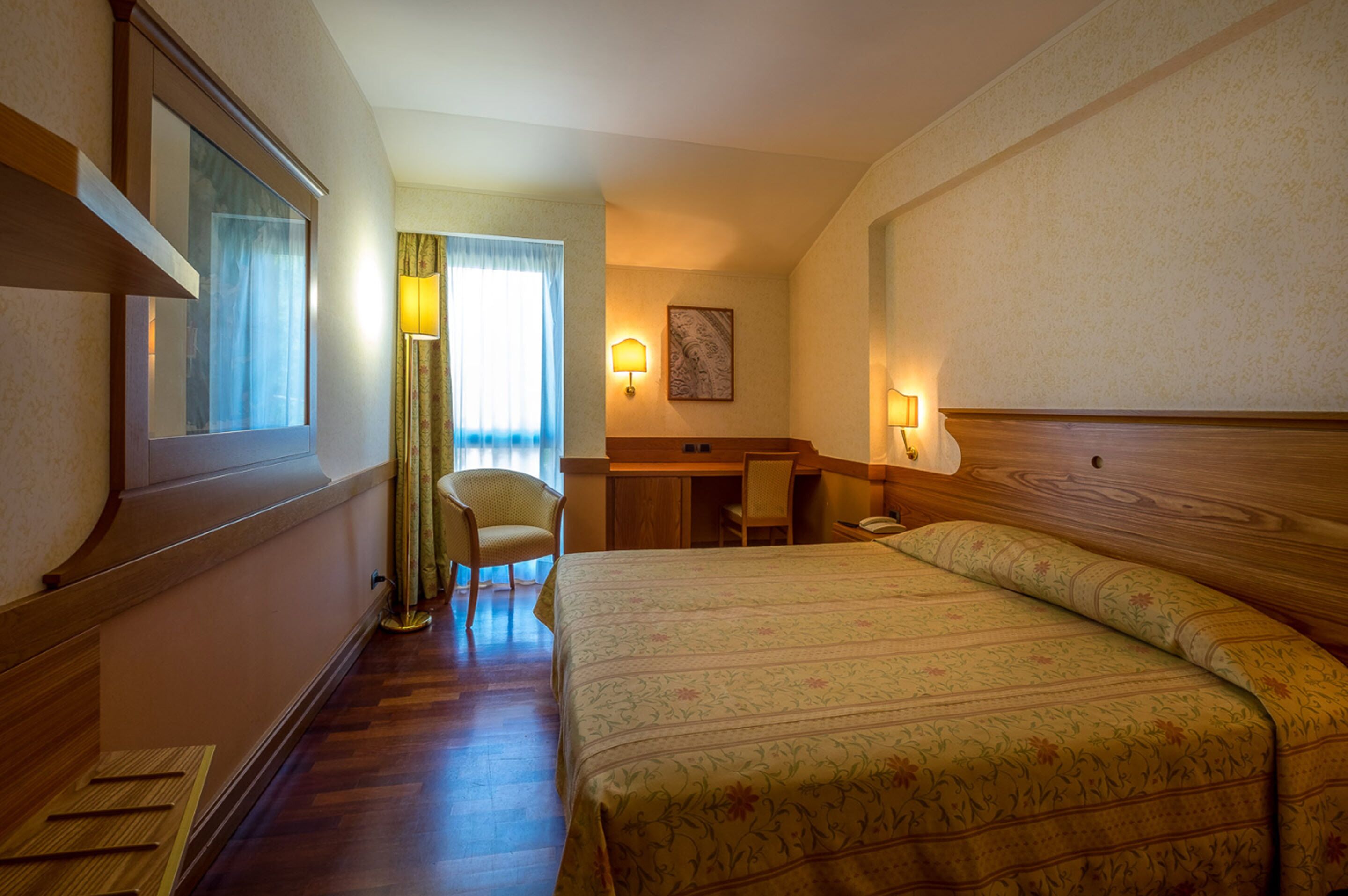 A hotel room with a bed, a desk, a chair, and a lamp.