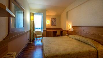 A hotel room with a bed, a desk, a chair, and a lamp.