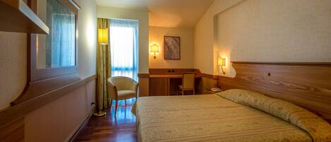 A hotel room with a bed, a desk, a chair, and a lamp.