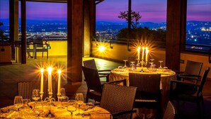 Un área de comedor al aire libre con mesas preparadas para dos, con centros de mesa iluminados por velas y sillas de mimbre.