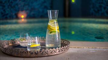 Un plateau avec une carafe et deux verres contenant une boisson claire agrémentée de rondelles de citron vert, placé au bord d’une piscine.