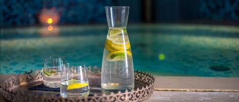 Una bandeja con una jarrón y dos vasos de una bebida transparente, adornada con rodajas de lima, colocada junto a una piscina.