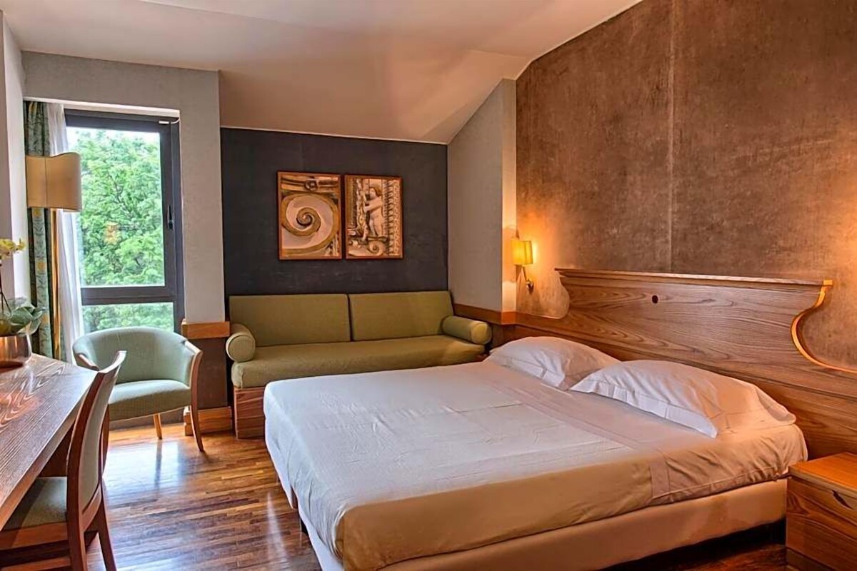 Una habitación de hotel con cama, sofá, mesa de comedor y lámpara.
