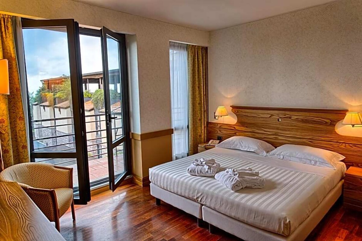 Habitación de hotel con una cama grande, una silla, un escritorio y vistas a través de un ventanal.