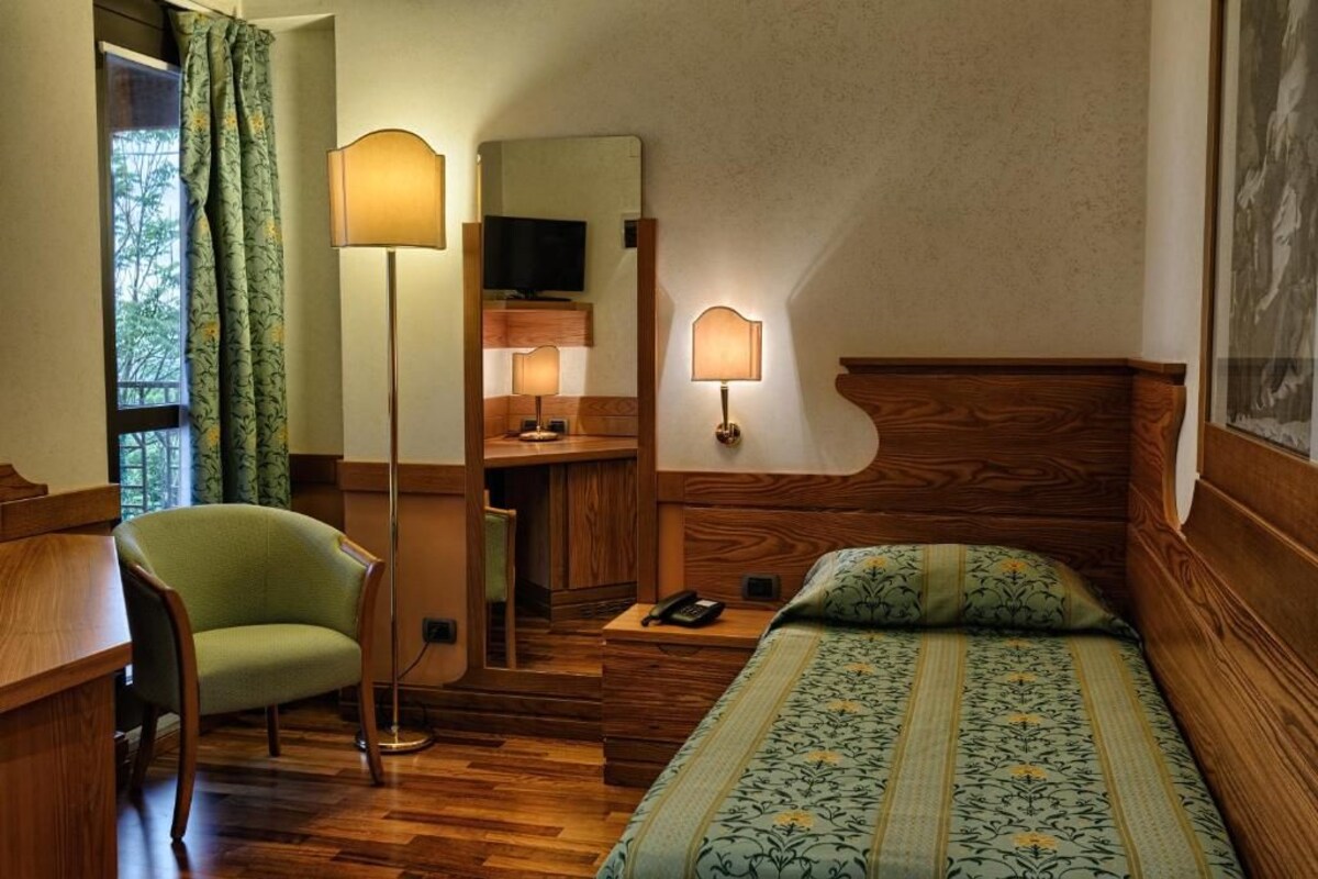 Una habitación de hotel con una cama de madera, un escritorio, una silla, una lámpara de escritorio, un teléfono y una televisión.