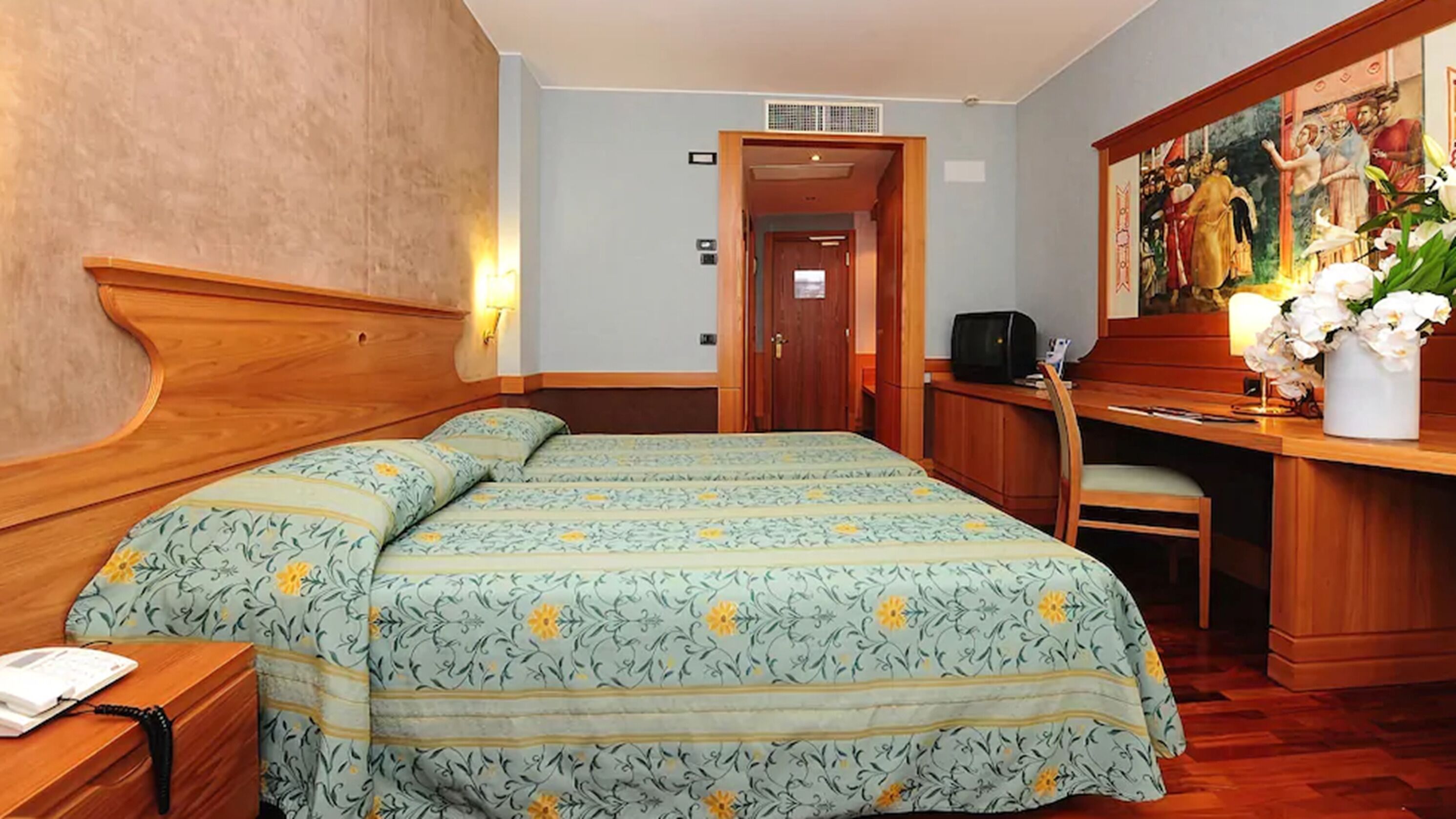 A hotel room with two beds, a desk with a chair, a telephone, and a painting on the wall.