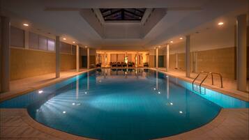 Una piscina interior con tragaluces, paredes de azulejos y una zona de estar al fondo.