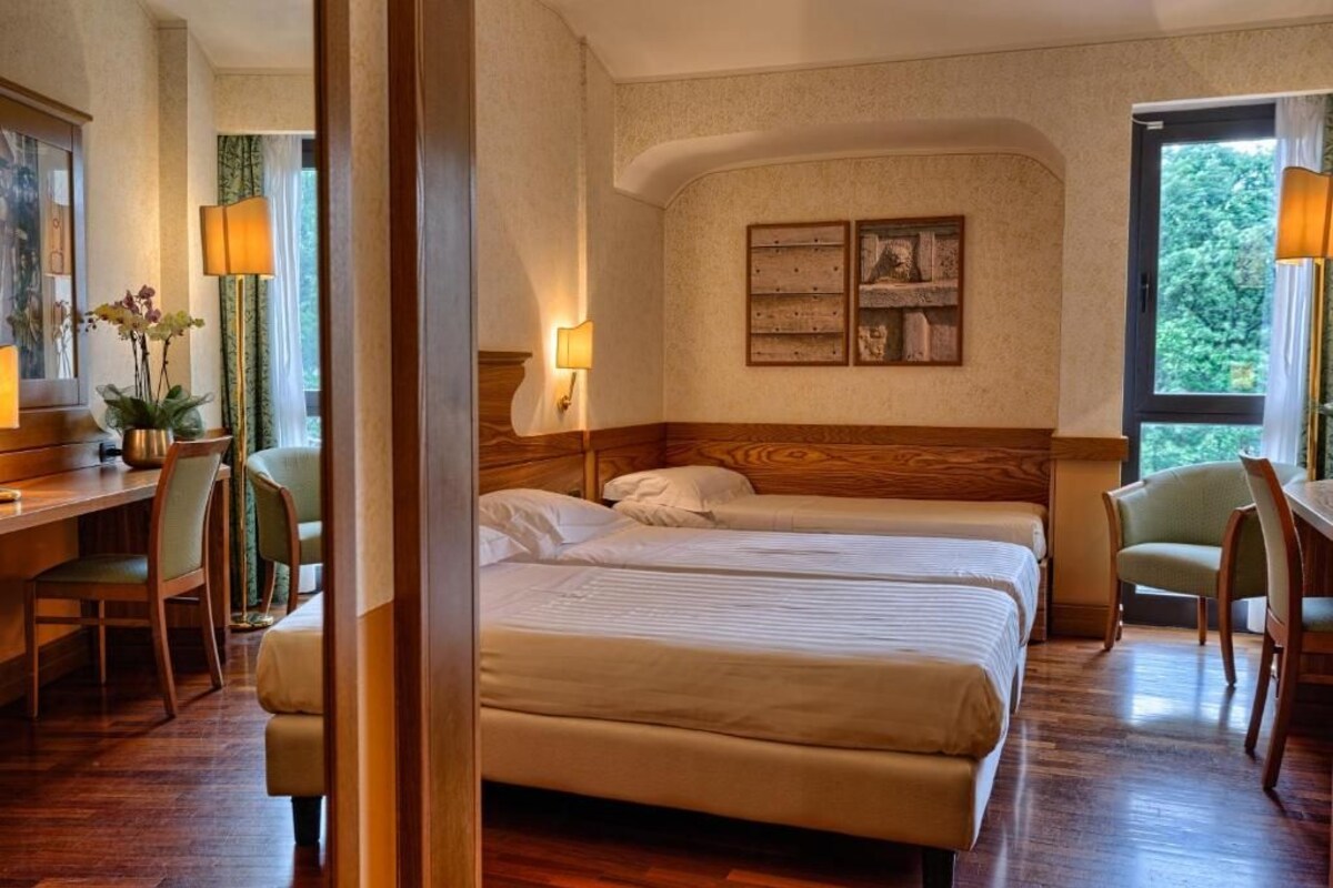 Habitación de hotel con dos camas, un escritorio, sillas y un ventanal grande.