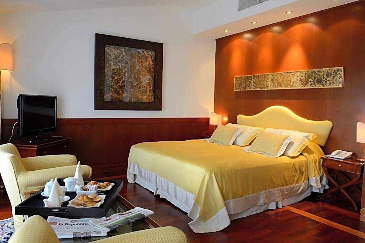 Una habitación de hotel con una cama grande, televisión, bandeja con productos de desayuno y obras de arte en las paredes.