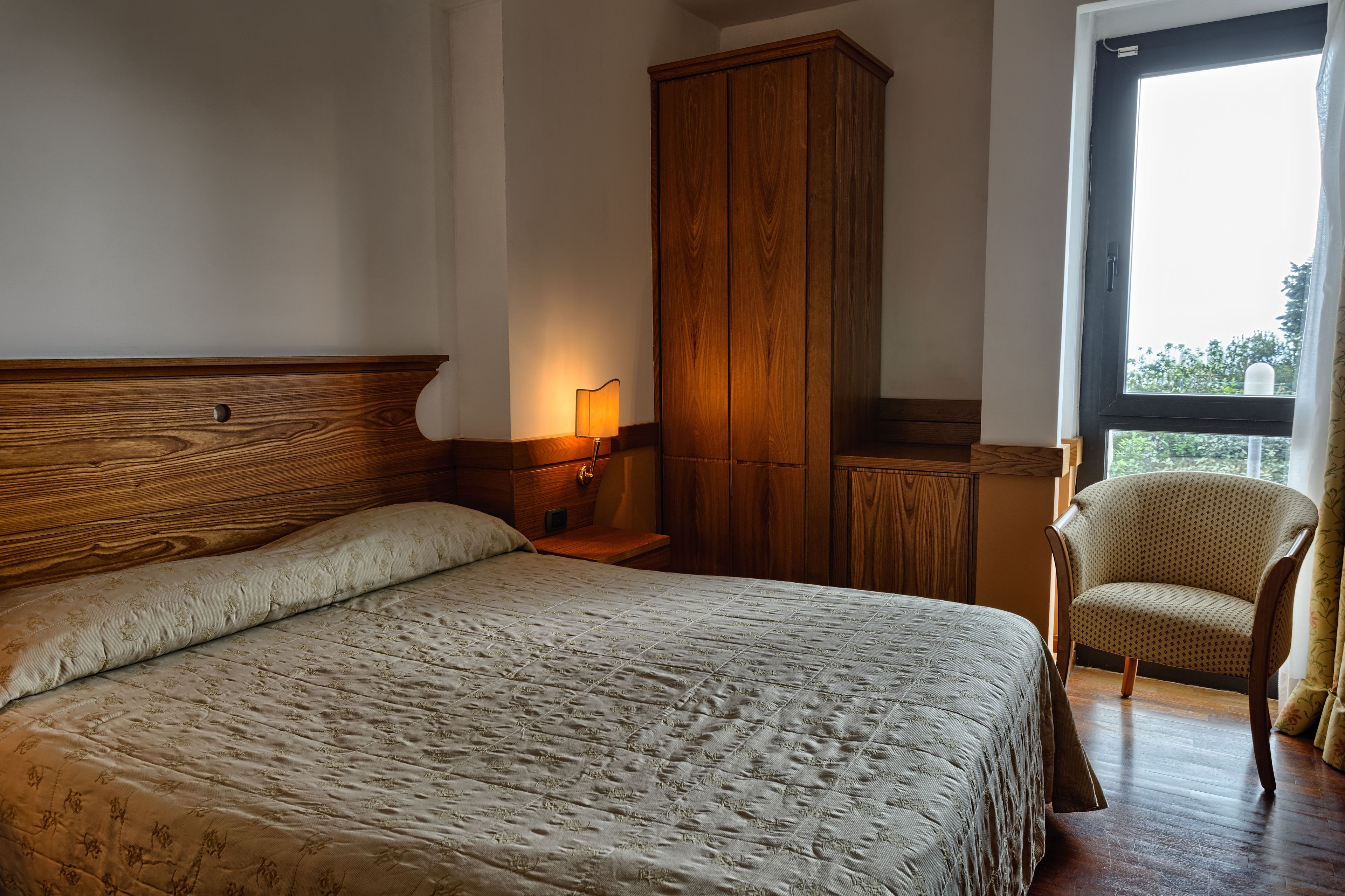 Un dormitorio con una cama grande, un armario de madera, una silla y una ventana con vistas.