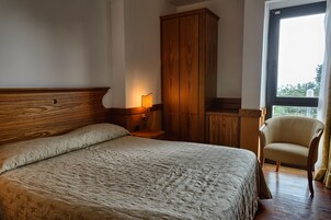 Un dormitorio con una cama grande, un armario de madera, una silla y una ventana con vistas.