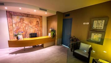 Zona de recepción con un escritorio de madera, una silla, un muro con un mosaico y una puerta.
