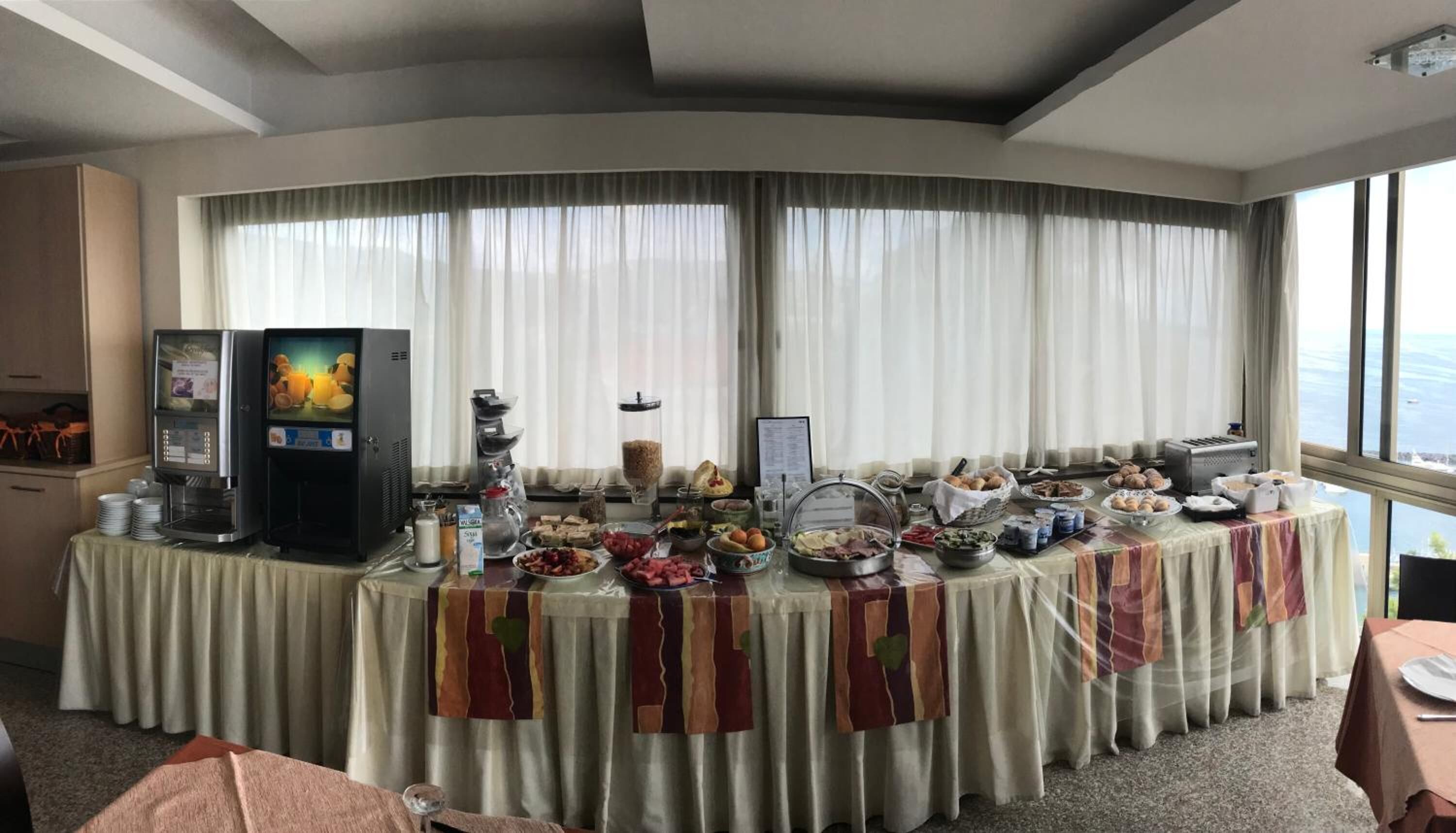 A breakfast buffet setup in a hotel room with a large window, a coffee machine, and various food items.
