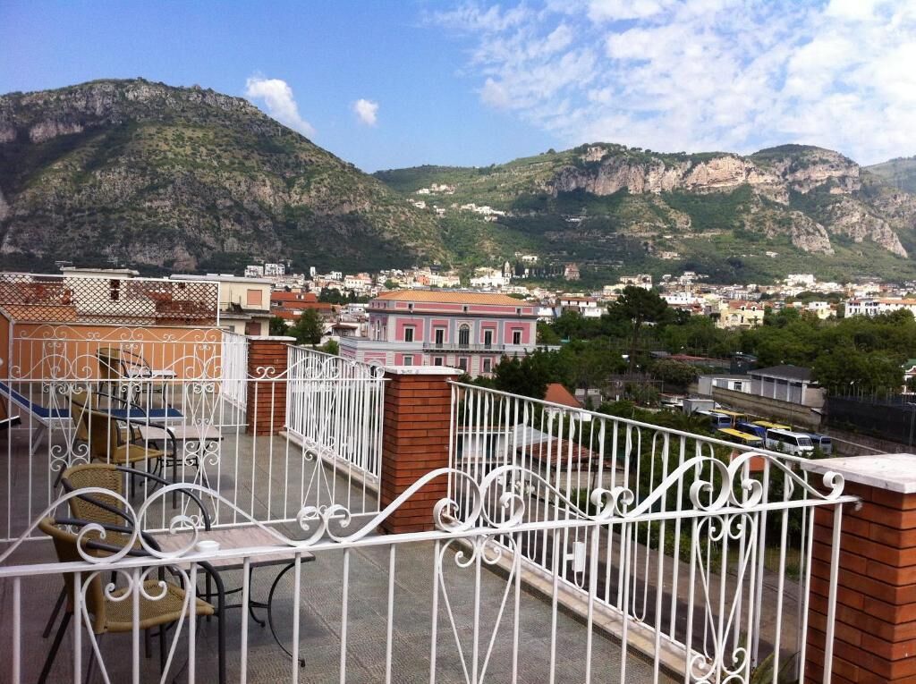 Ein Balkon mit Metallgeländern, einer Backsteinmauer und Blick auf eine Stadt mit Gebäuden und Bergen im Hintergrund.