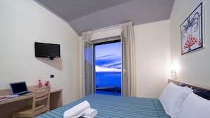 Habitación de hotel con cama, escritorio con una computadora portátil, televisión y balcón con vistas.