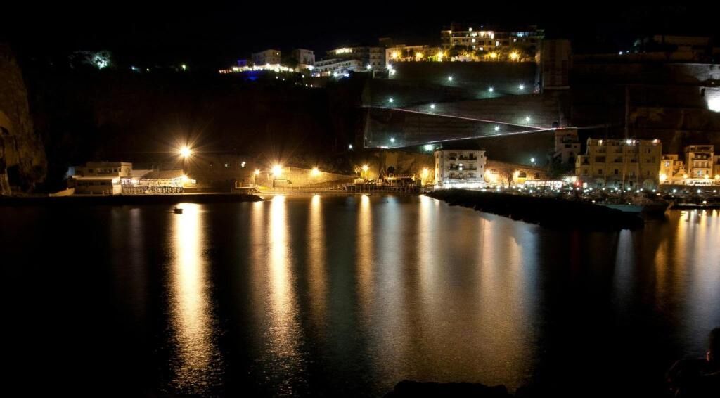 A coastal town at night with illuminated buildings and a calm sea.