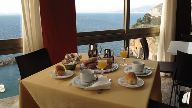 Una mesa lista para el desayuno con vista al mar y acantilados.