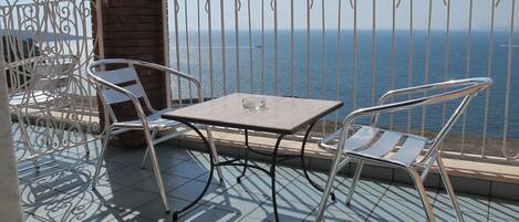 A balcony with a table and chairs, overlooking a body of water.