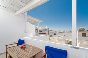 A balcony with a wooden table, two chairs, and a view of the sea and buildings. - Antonia Studios (Naxos)