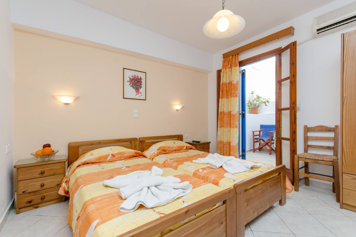 A bedroom with two wooden beds, a nightstand with a fruit bowl, a chair, and a wardrobe.
