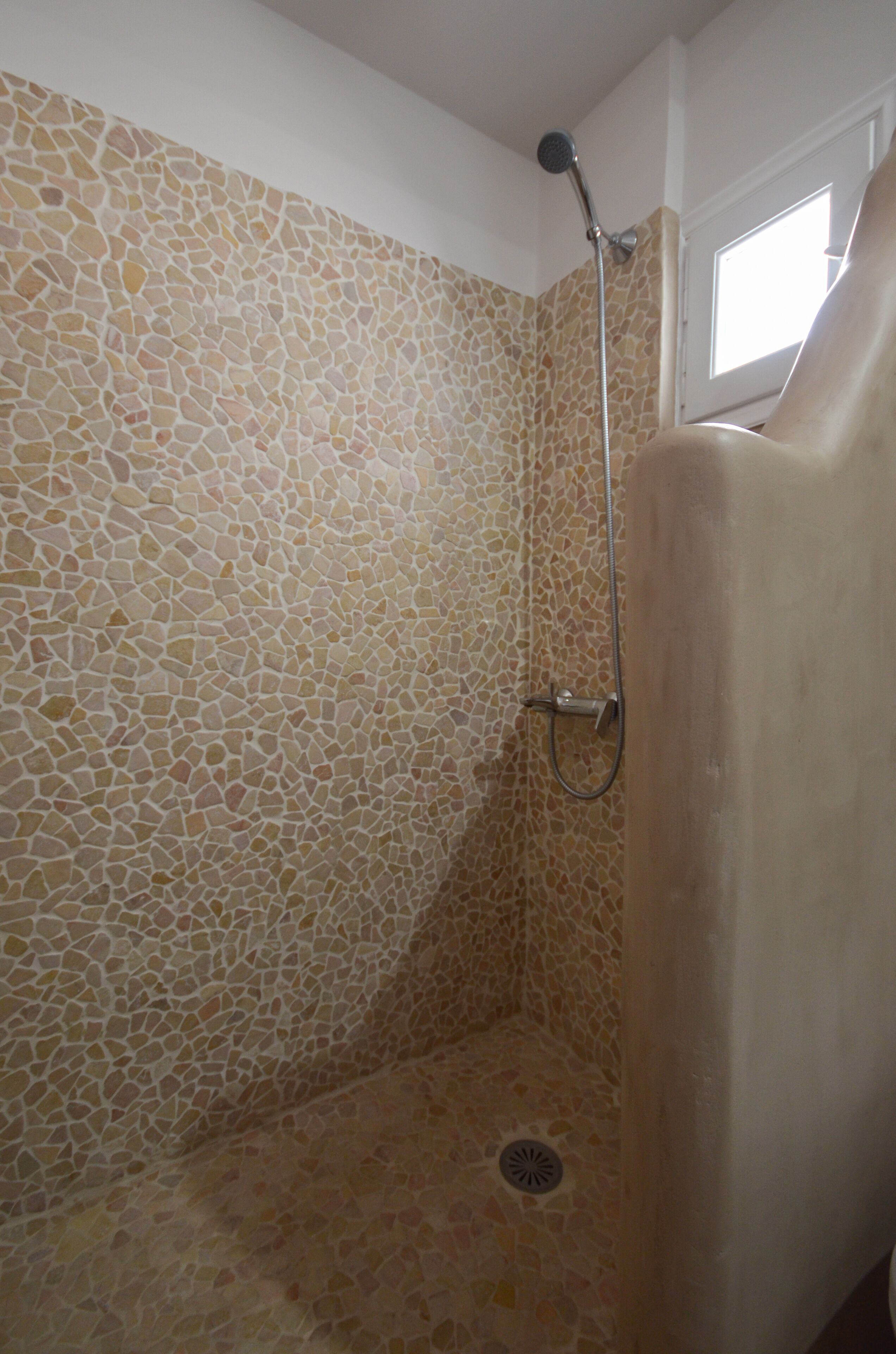 A shower with mosaic tile walls and a window above.
