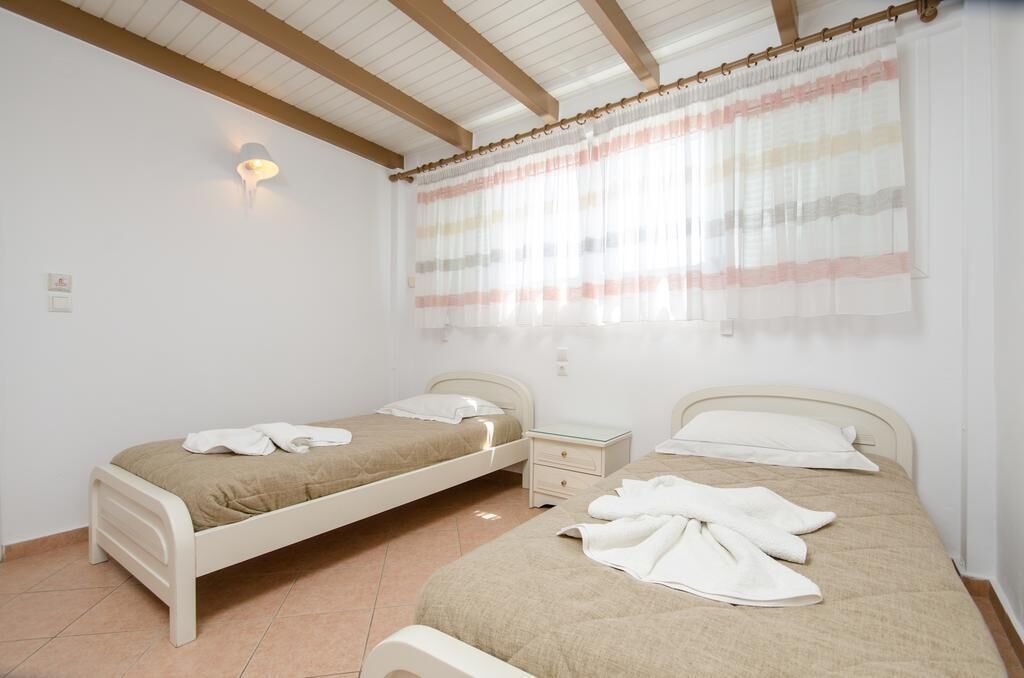 A bedroom with two beds, a nightstand, a lamp, and a window with curtains.