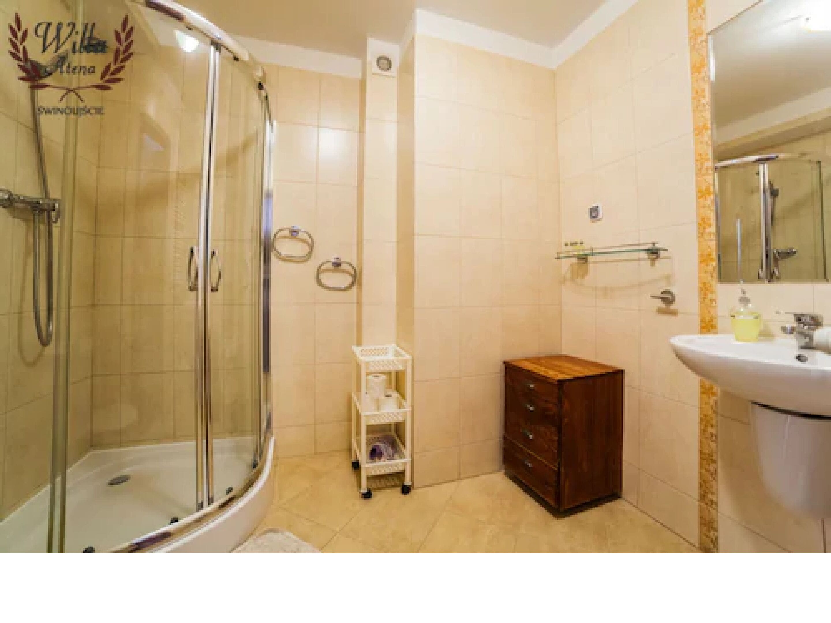 A bathroom with a glass-enclosed shower, a wooden cabinet, a sink, and a small white shelf with toiletries.