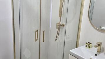 Ein modernes Badezimmer mit einer ein Glasabdeckung tragenden Dusche, einem weißen Waschbecken mit goldfarbenen Armaturen und einem Spiegel über dem Waschbecken.