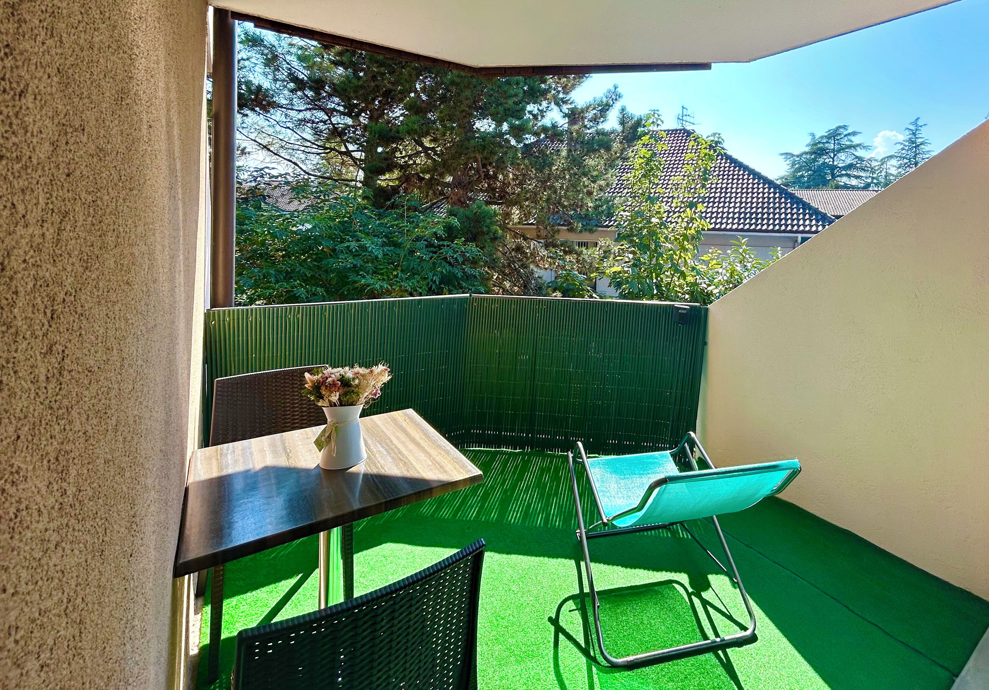 A small balcony with a table, chairs, and a potted plant.