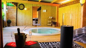 A wooden spa area with a hot tub, a bottle of champagne, and a glass of wine on a mat. - Résidence les Thermes Côté Chalet (Thonon-les-Bains)