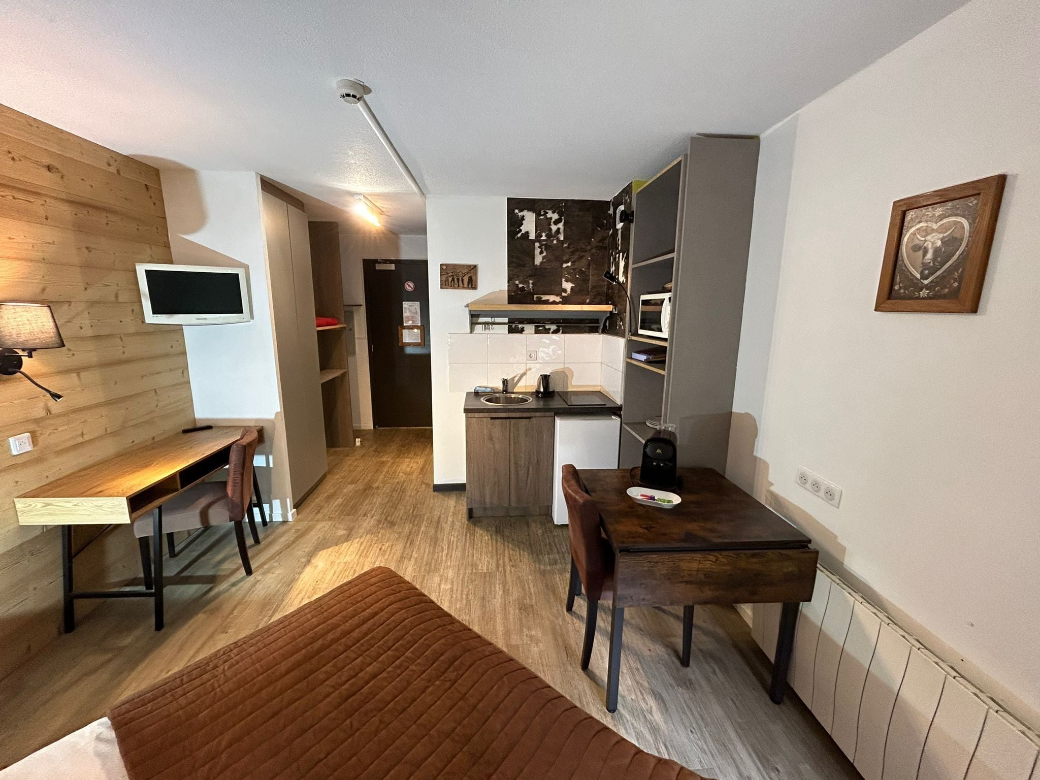 A compact living space with a kitchenette, a dining area, and a TV mounted on the wall.