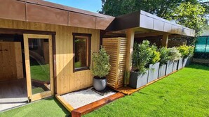 A modern building with wooden exterior walls, large sliding glass doors, and a small garden area with potted plants. - Résidence les Thermes Côté Chalet (Thonon-les-Bains)