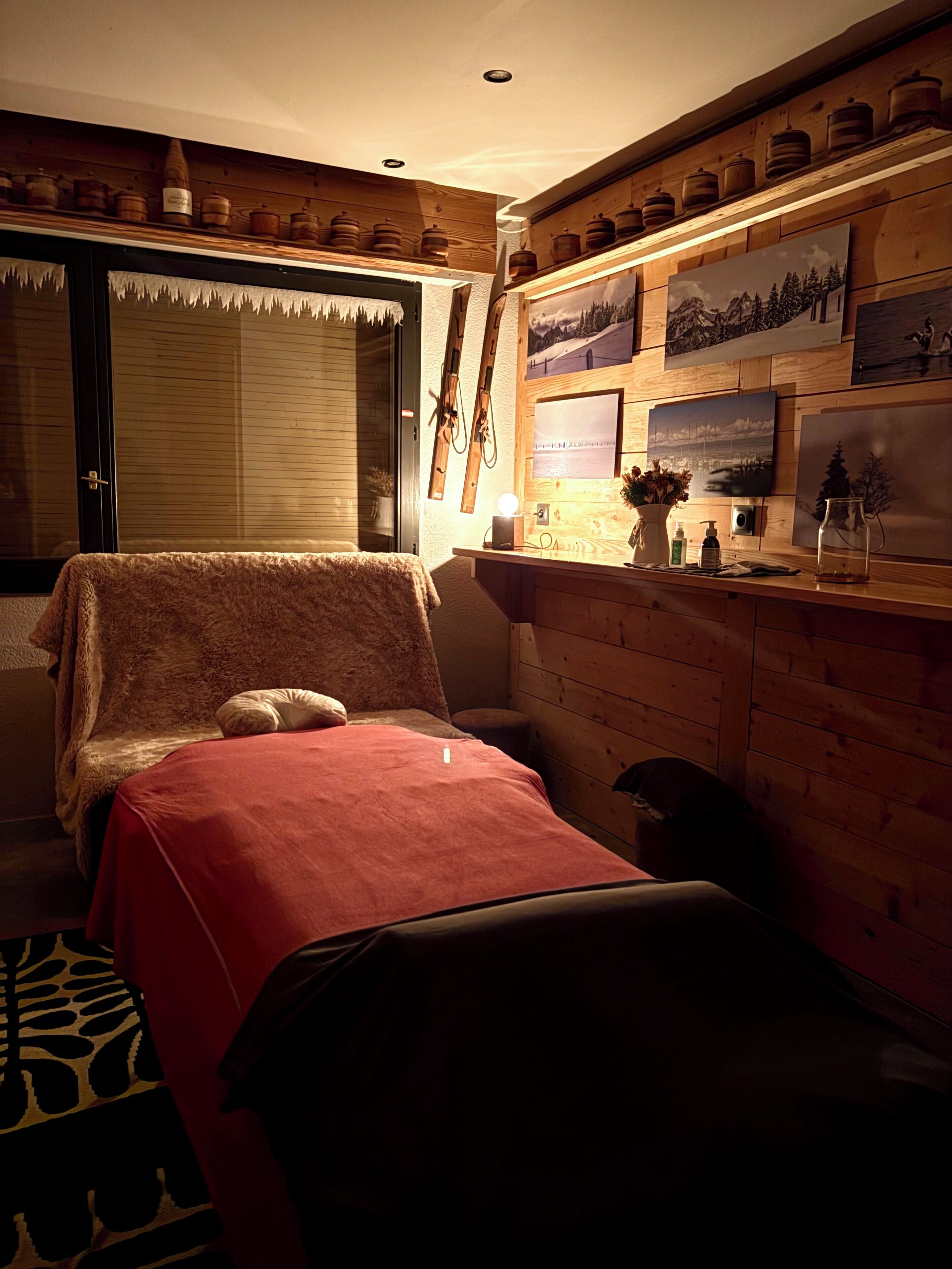 A cozy room with a bed, wooden shelves with jars, and framed pictures on the wall.