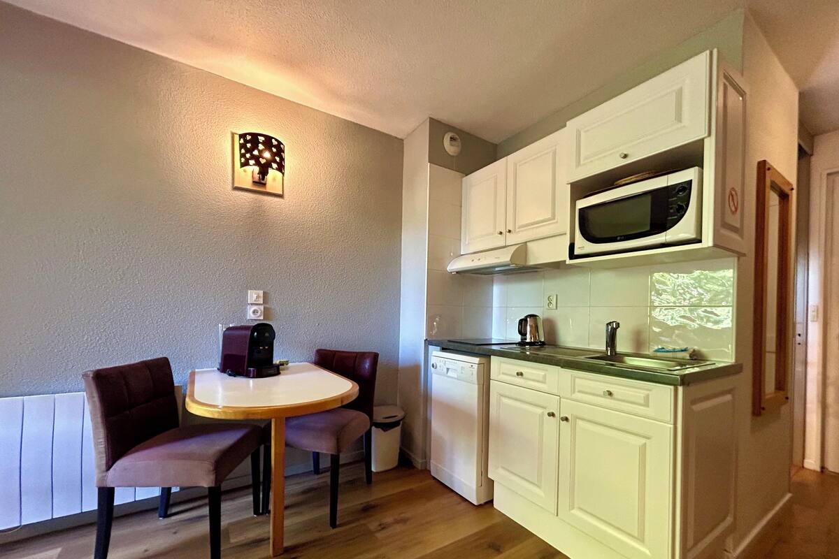 A compact kitchen with white cabinets, a microwave, a dishwasher, and a dining table with two chairs.