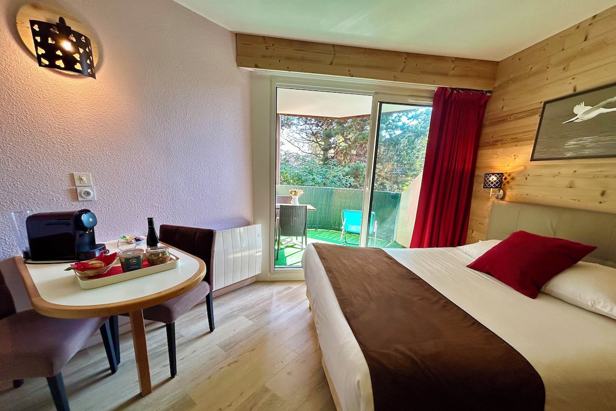 A bedroom with a bed, a table with a coffee maker, and a view of the outside.