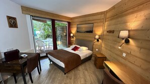 A wooden-paneled room with a bed, a desk, and a chair. There is a view through a glass door to an outdoor area with chairs. - Résidence les Thermes Côté Chalet (Thonon-les-Bains)
